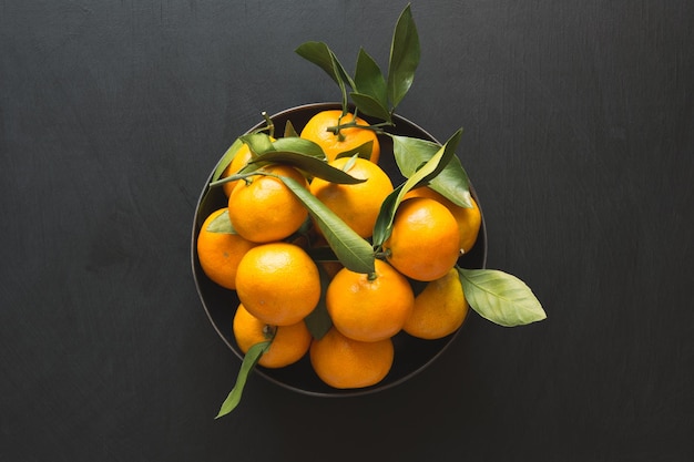 Fresh mandarins with leaves in bowl on black Healthy eating concept Copy space