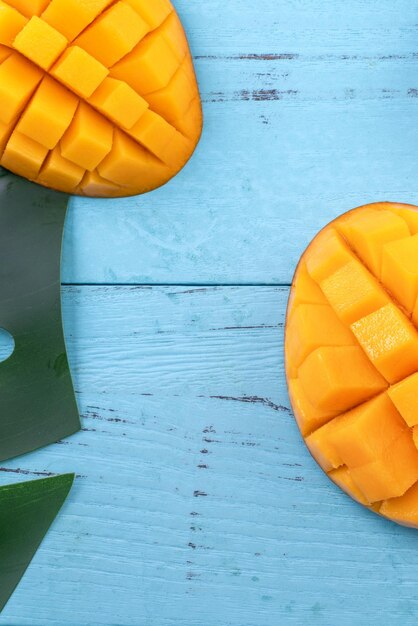 Photo fresh mango beautiful chopped fruit with green leaves on bright blue timber background tropical fruit design concept flat lay top view copy space