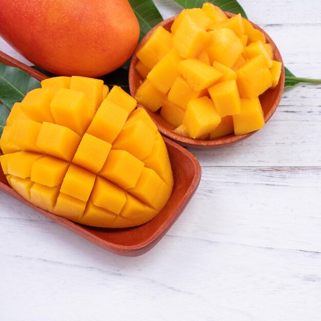 Fresh mango,beautiful chopped fruit with green leaves on bright wooden table background. tropical fruit design concept, close up, copy space