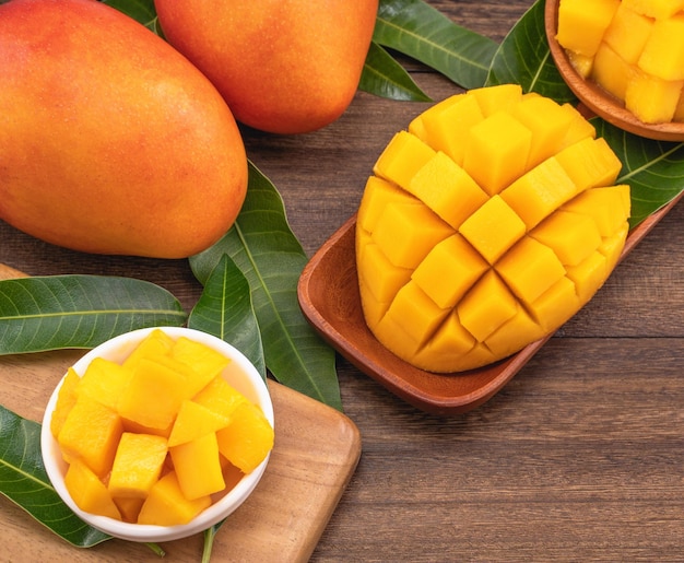 Fresh mango beautiful chopped fruit with green leaves on dark wooden table background Tropical fruit design concept Flat lay Top view Copy space