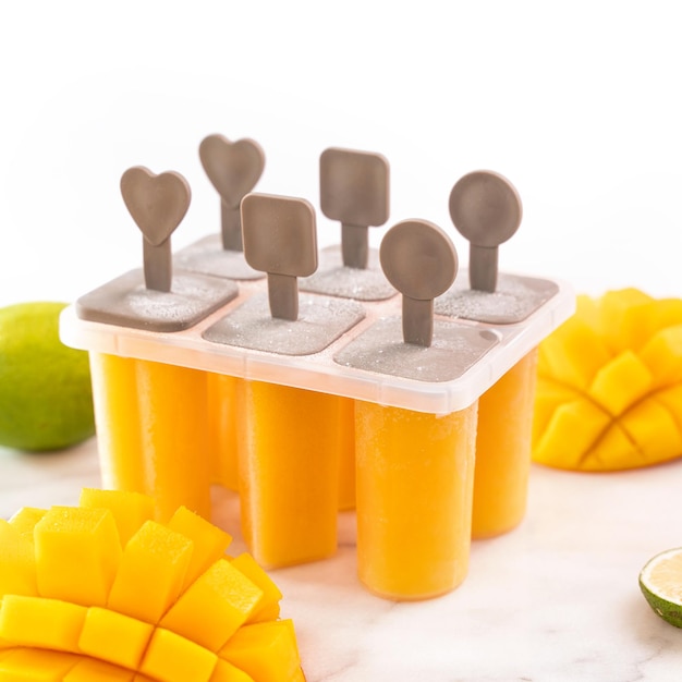 Fresh mango fruit popsicle ice in the plastic shaping box on bright marble table Summer mood concept product design close up