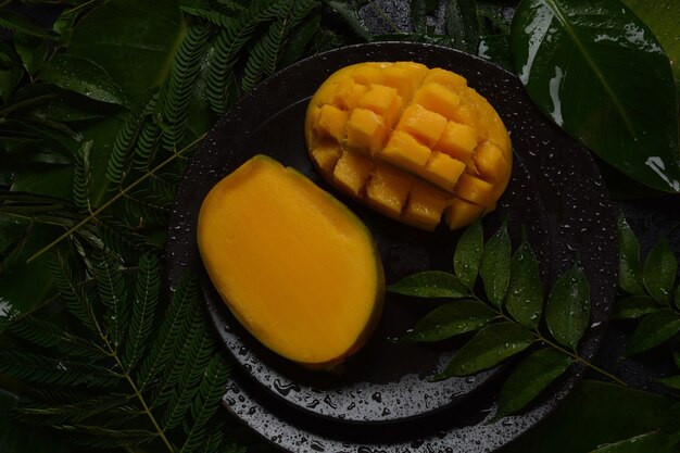 Fresh mango fruit with sliced diced mango chunks on a plate or on leaves as a background