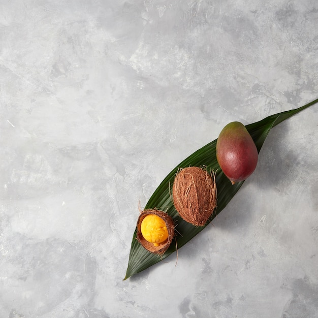 新鮮なマンゴー、ココナッツ全体、ココナッツの殻、ヤシの葉に黄色いアイスクリーム、灰色のコンクリートの背景にテキスト用のスペースがあります。フラットレイ