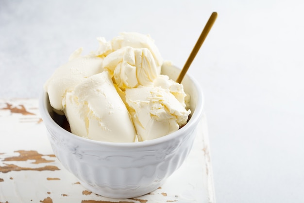 Fresh mascarpone cheese in a white bowl for making Italian tiramisu dessert on light background. Selective focus.