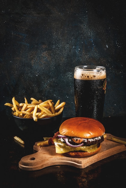 Fresh meat and cheese burger with French fries and glass of dark ginger beer, on dark blue , 