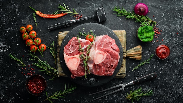 Fresh meat Ossobuko steak on the bone with rosemary and spices On a black stone background Top view