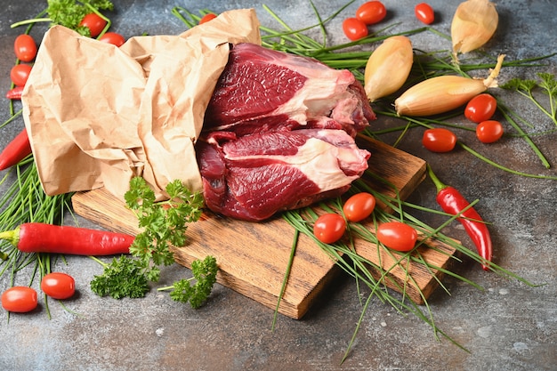Свежее мясо с ингредиентами для приготовления пищи на коричневой деревянной разделочной доске.
