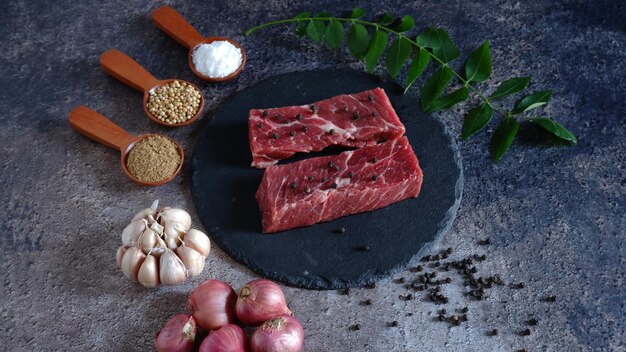 写真 黒い皿と暗い背景にいくつかの食材を載せた新鮮な肉