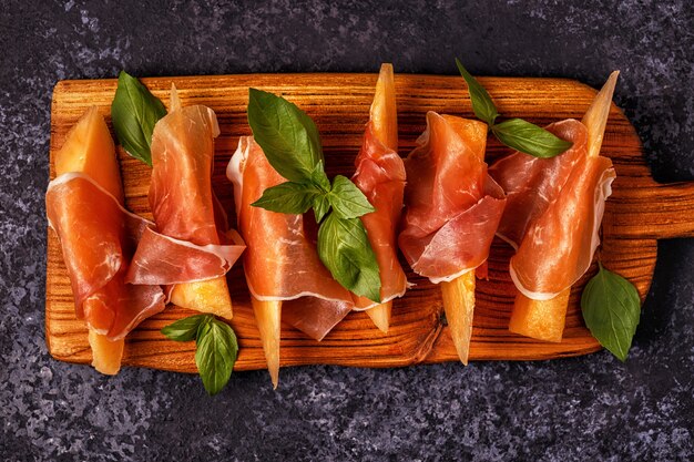 Foto melone fresco con prosciutto e basilico su una tavola di legno