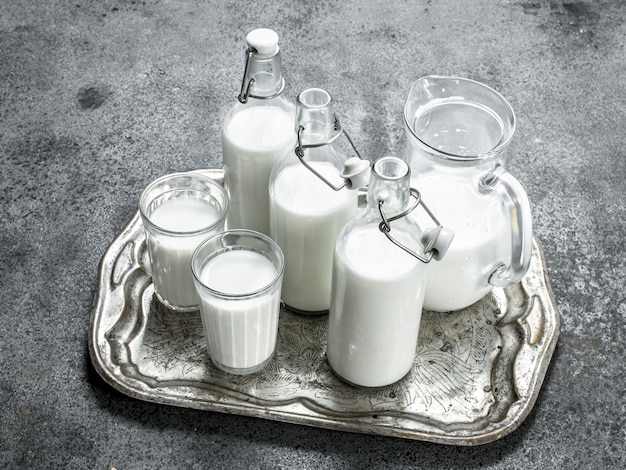 Photo fresh milk in bottles, jugs and glasses on a steel tray.