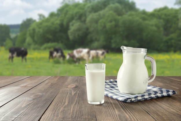 暗い木製のテーブルと牧草地で牛とぼやけた風景のガラスの新鮮な牛乳。健康的な食事。素朴なスタイル。