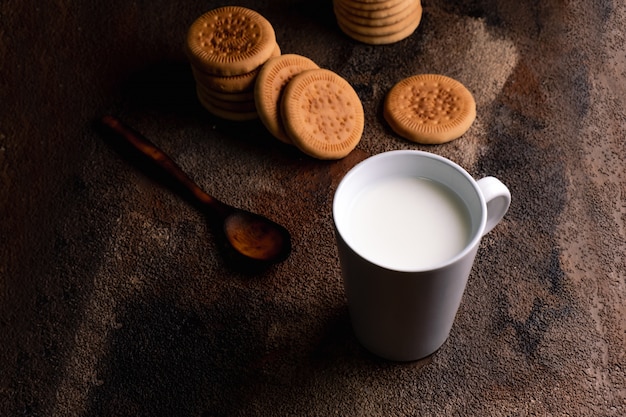 Foto latte fresco con i biscotti fatti in casa su un tavolo di legno, sfondo scuro.