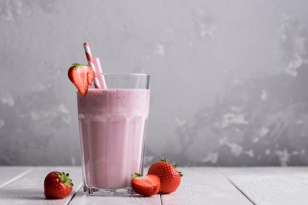 Fresh milkshake with strawberries on a light table.