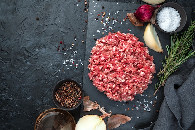 Fresh minced meat with onion and rosemary on a black background.