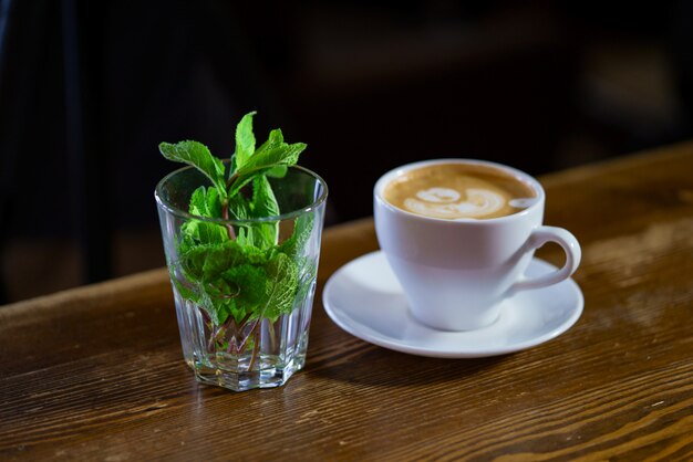 Fresh mint in a glass and a cup of latte art coffee on a wooden table.