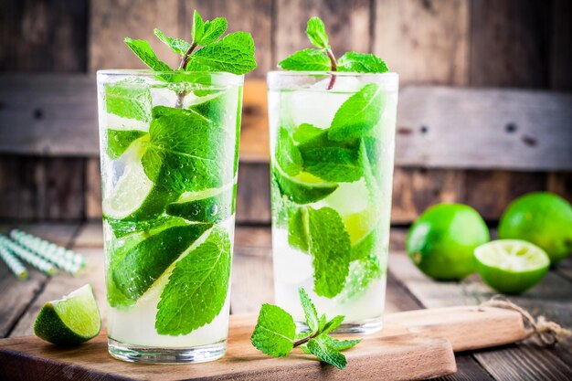 Fresh mojito cocktails with lime mint and ice in glass on wooden background