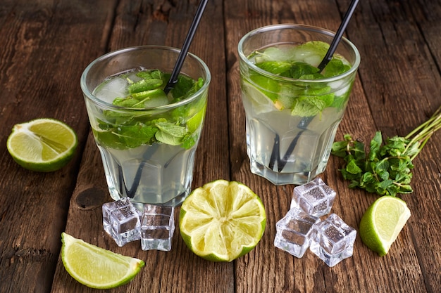 Fresh mojito in glasses with ice cubes on wooden table.