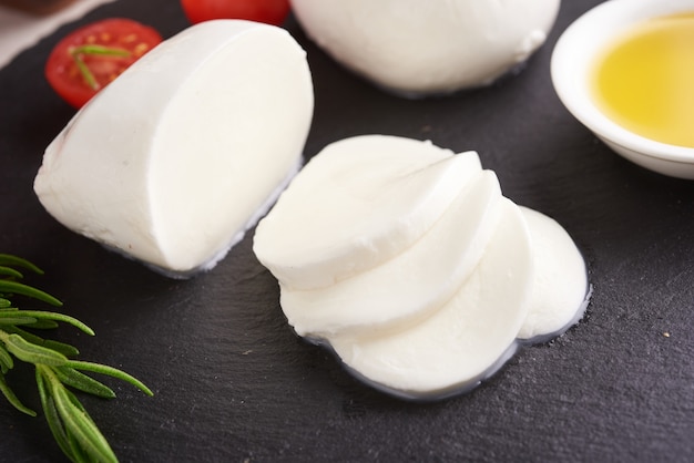 Fresh mozzarella cheese, Soft italian cheeses, tomato and basil, olives oil and rosemary on wooden serving board over light wooden surface. Healthy food. Top view. Flat lay.