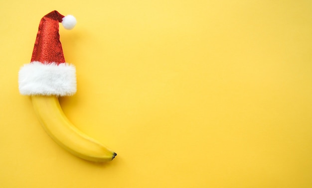 Frutta fresca banana naturale in un cappello di babbo natale rosso su sfondo giallo. buon natale