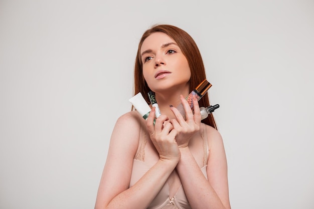 Fresh natural beautiful young redhead girl in a bra holds a cosmetic product and takes care of her skin