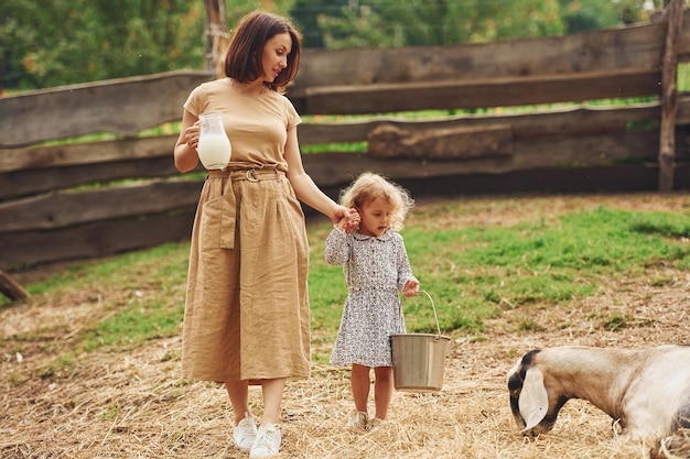 Latte fresco naturale la giovane madre con sua figlia è nella fattoria in estate con le capre