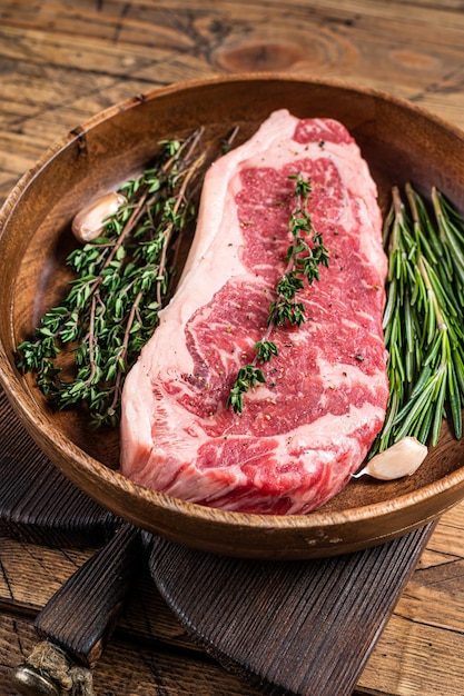 Fresh new york strip beef meat steak or striploin in a wooden plate with herbs. wooden background. Top view.