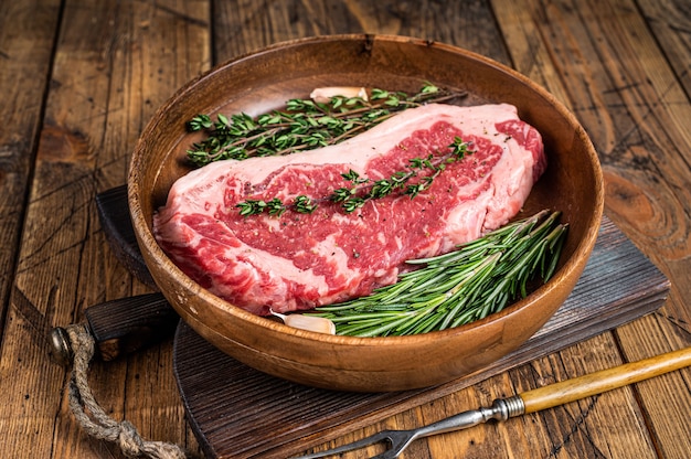 Fresh new york strip beef meat steak or striploin in a wooden plate with herbs