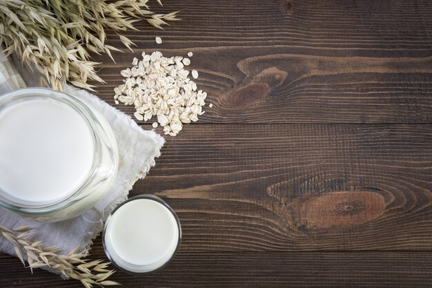 Fresh oat milk in glass and pitcher on dark wooden table background. Healthy eating. Rustic style.