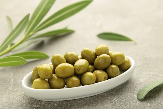 Fresh olives in bowl with leaves on grey background with copy space.