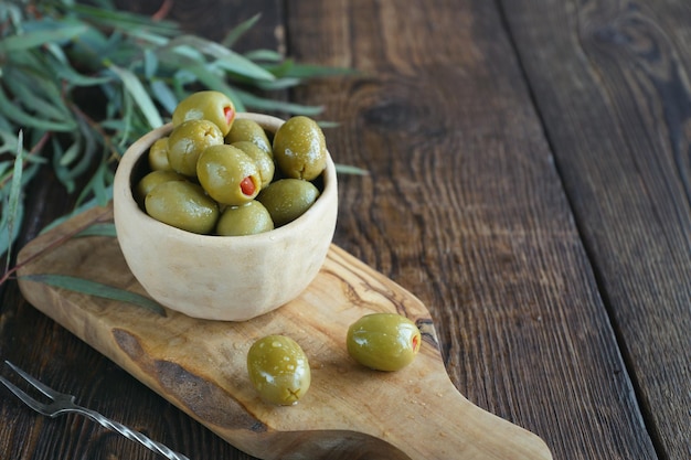fresh olives in ceramic bowl and vintage fork on board on a dark rustic wooden background. olives on olive wood.