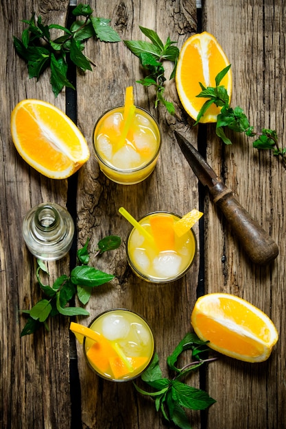Свежий апельсиновый коктейль отвертка. Апельсиновый коктейль с алкоголем, льдом и листьями мяты на деревянном столе. Вид сверху