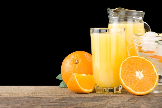 Свежий апельсиновый сок в стакане и кусочки, изолированные на черном фоне