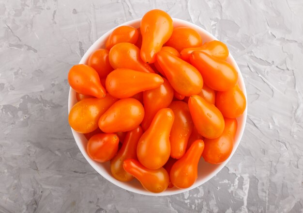 회색 콘크리트 표면에 흰색 세라믹 그릇에 신선한 오렌지 포도 토마토. 평면도.