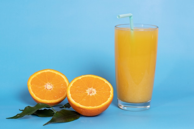 Succo d'arancia fresco in un bicchiere con frutta tagliata a metà e affettata in foglie verdi isolate su un blu