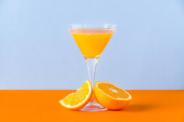 Fresh orange juice in a glass with a slice and a half at the base on an orange surface