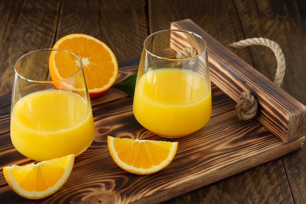 Fresh orange juice in glasses with cut oranges on wooden tray. Rustic still life with citrus fruits.