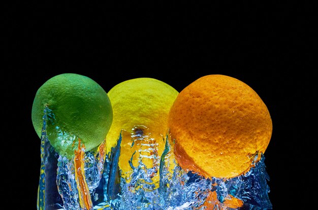 Fresh orange, lyme, lemon falling in water with splash on black background