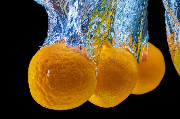 Photo fresh orange, mandarine falling in water with splash on black