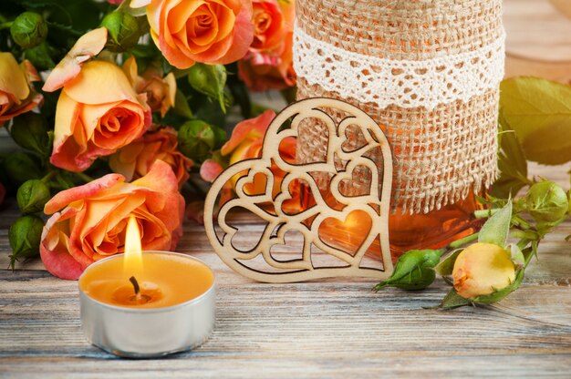 Fresh orange roses flowers, heart, decor bottle and lit candle