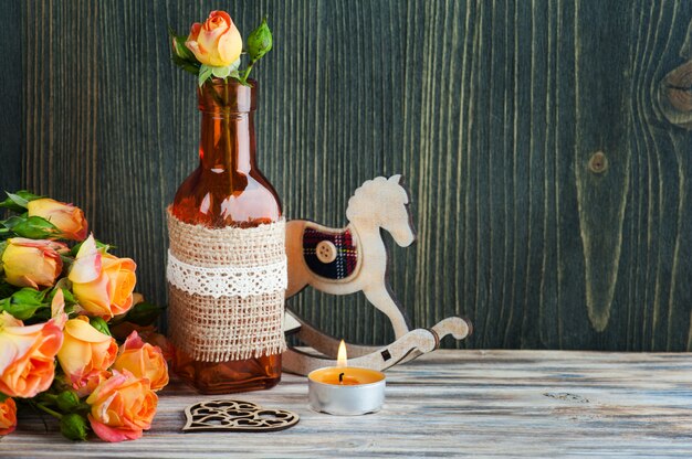 Fresh orange roses flowers, heart, decor bottle and lit candle