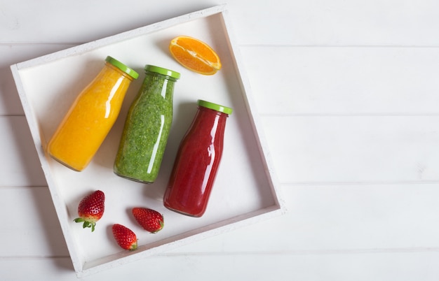 Fresh orange, strawberry and broccoli smoothie in bottles with fruits and mint in a white wooden rustic box