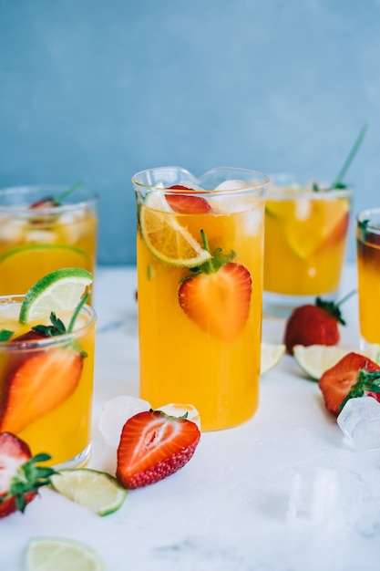 Fresh orange strawberry mojito in different glasses with ice cubes and slices of lime on the table