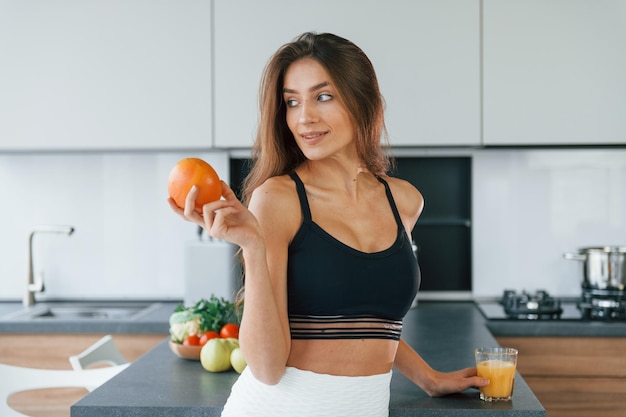 Fresh orange Young european woman is indoors at kitchen indoors with healthy food