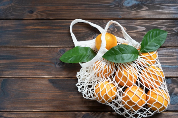 Fresh oranges in eco mesh bag on wooden table