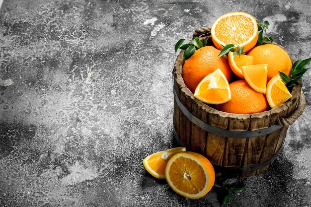 Fresh oranges in a wooden bucket on a rustic table.