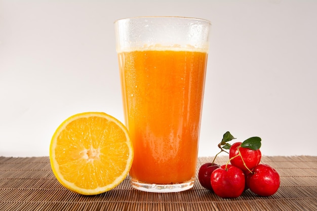 Fresh Organic Acerola and Orange Juice in a glass cup with half orange and acerola berries inside a wood basket in a white clean studio photo in front view
