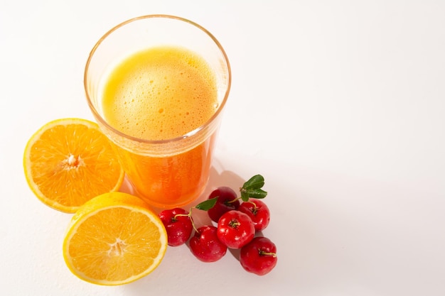Свежий органический ацерола и апельсиновый сок в стеклянной чашке с половиной апельсина и ягодами ацеролы на белом чистом студийном фото, вид сверху