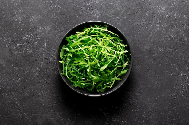 Fresh organic arugula  in  bowl on black background. Top view.