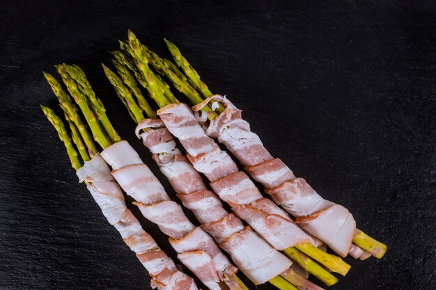 Fresh organic asparagus wrapped with bacon on a cutting board top view