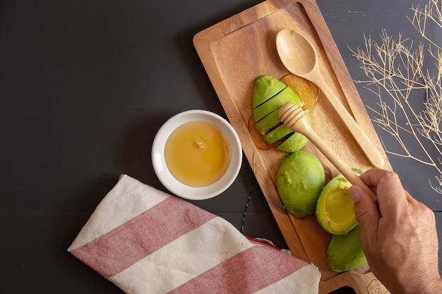 Fresh organic avocado sliced in half and honey on black wooden table.